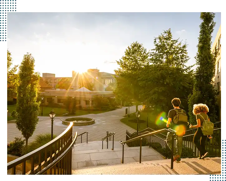 A scenic college campus with students walking down stairs and historic buildings in the background.